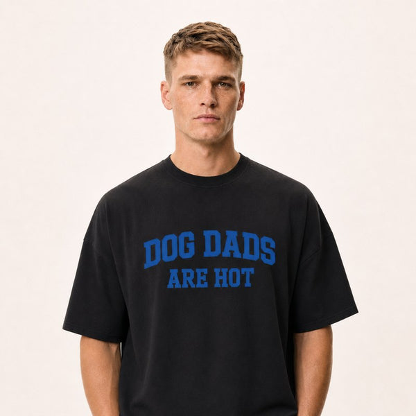 A model wearing a black tee printed with Dog Dads Are Hot in blue varsity type.