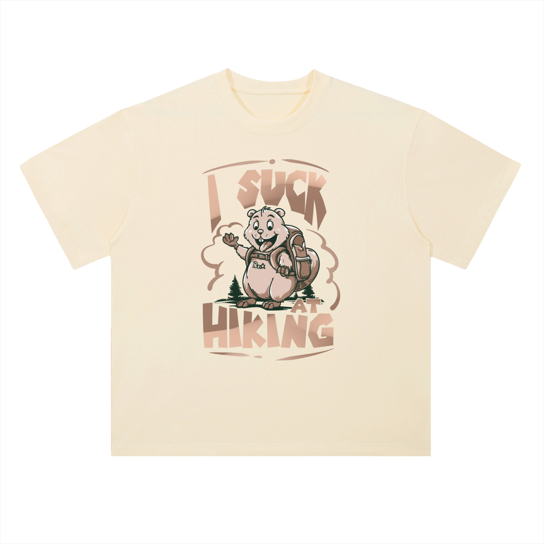 I Suck At Hiking Funny Cartoon Bear Tee in Milk Apricot, flat lay.