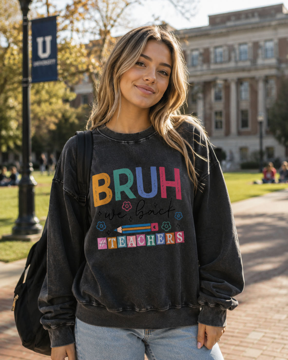 Bruh We Back Teacher Washed Sweatshirt in Black, worn with jeans on a university campus.