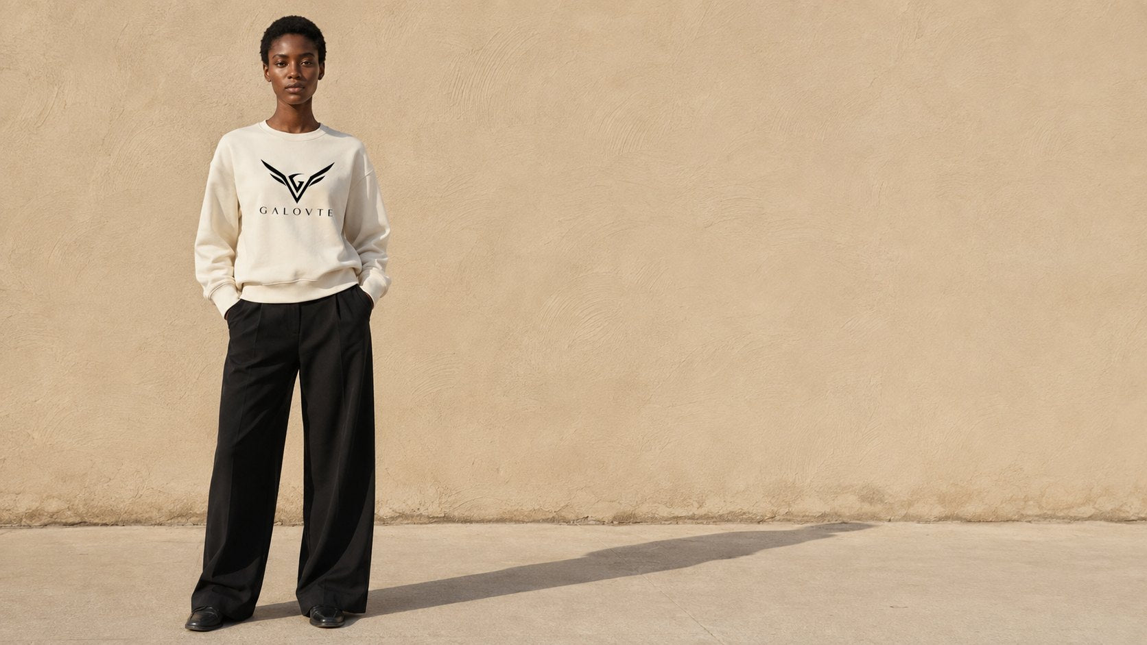 Translation missing: en.Model in a bone GALOVTE logo sweatshirt against a sunlit sand-coloured wall