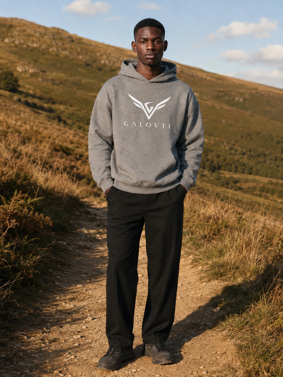 Model in a grey GALOVTE logo hoodie on a hillside walking trail