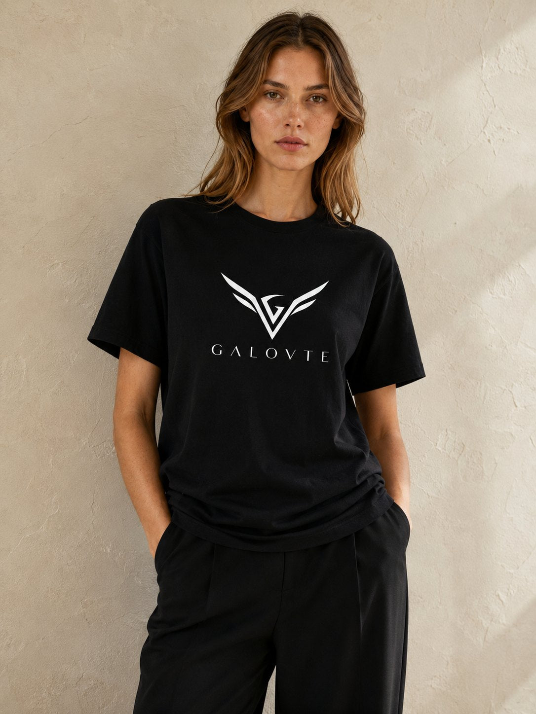Model in a black GALOVTE logo t-shirt against a warm plaster wall